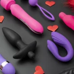 Plusieurs sextoy posés sur une table noire avec des petits coeurs rouge autour